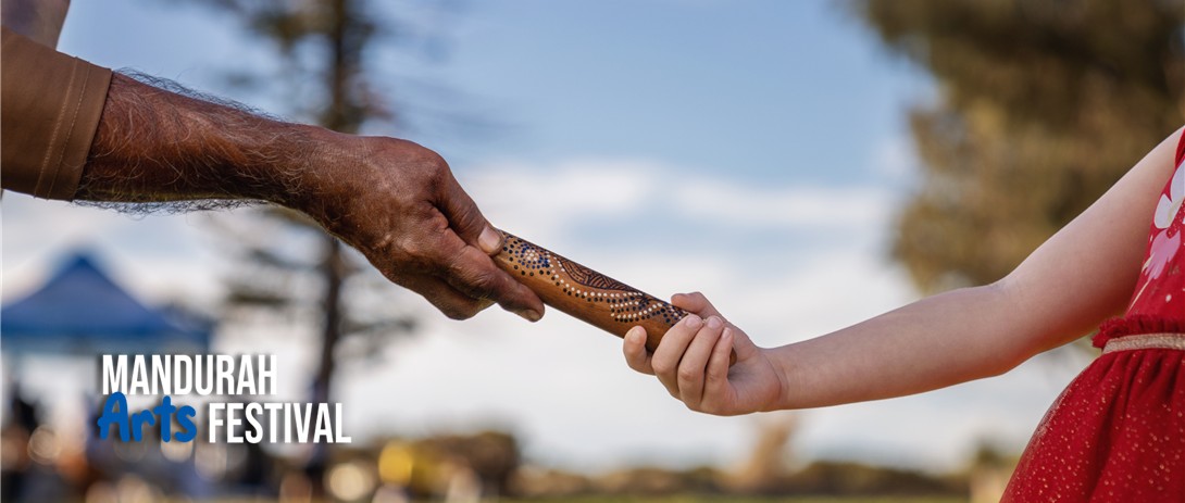The arm of an aboriginal man and the arm of a young caucasian girl both clasp a message stick from either end